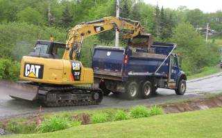 Cat backhoe digging a ditch and dumping the debris into a Halifax Water truck to be removed